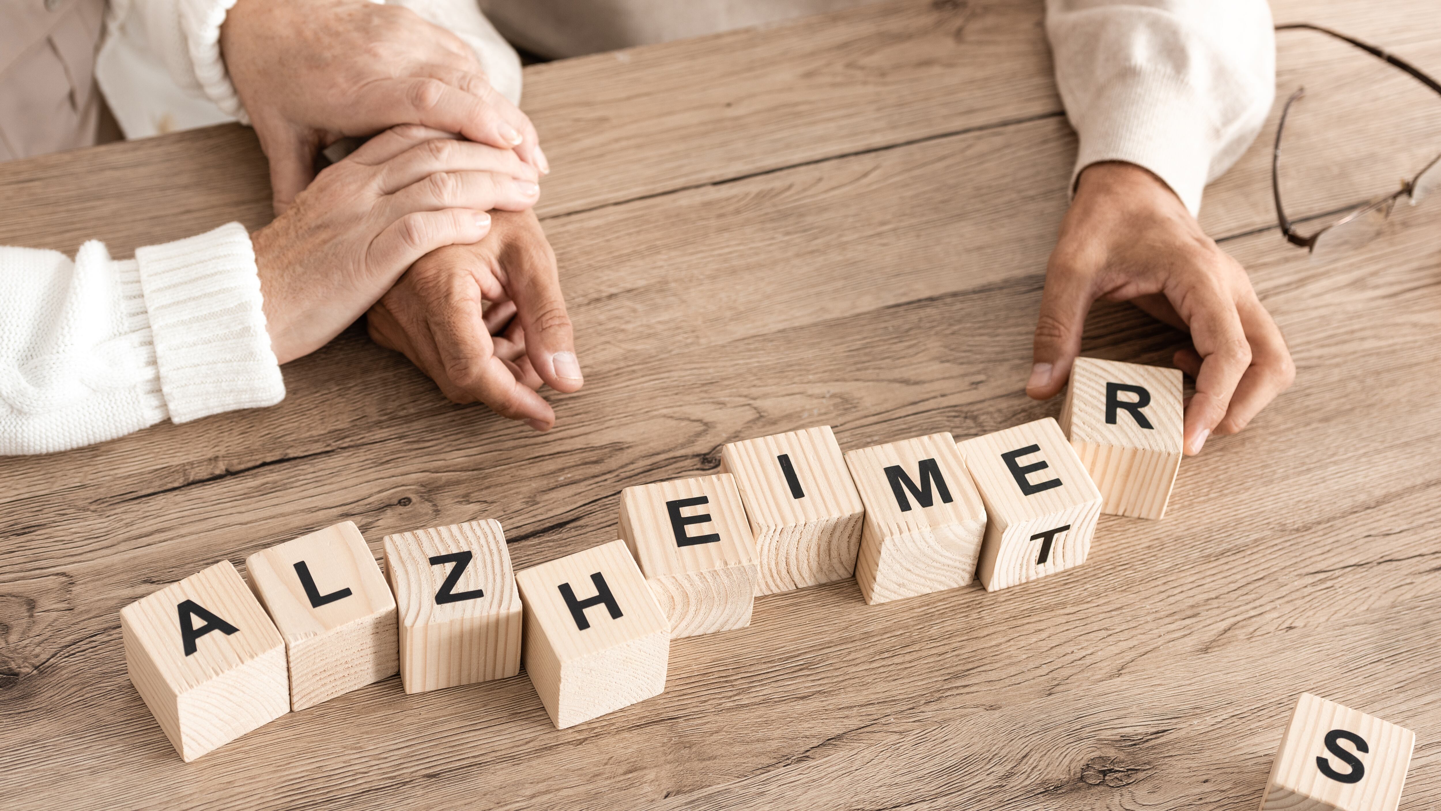 cropped view of retired couple sitting near wooden cubes with alzheimer letters